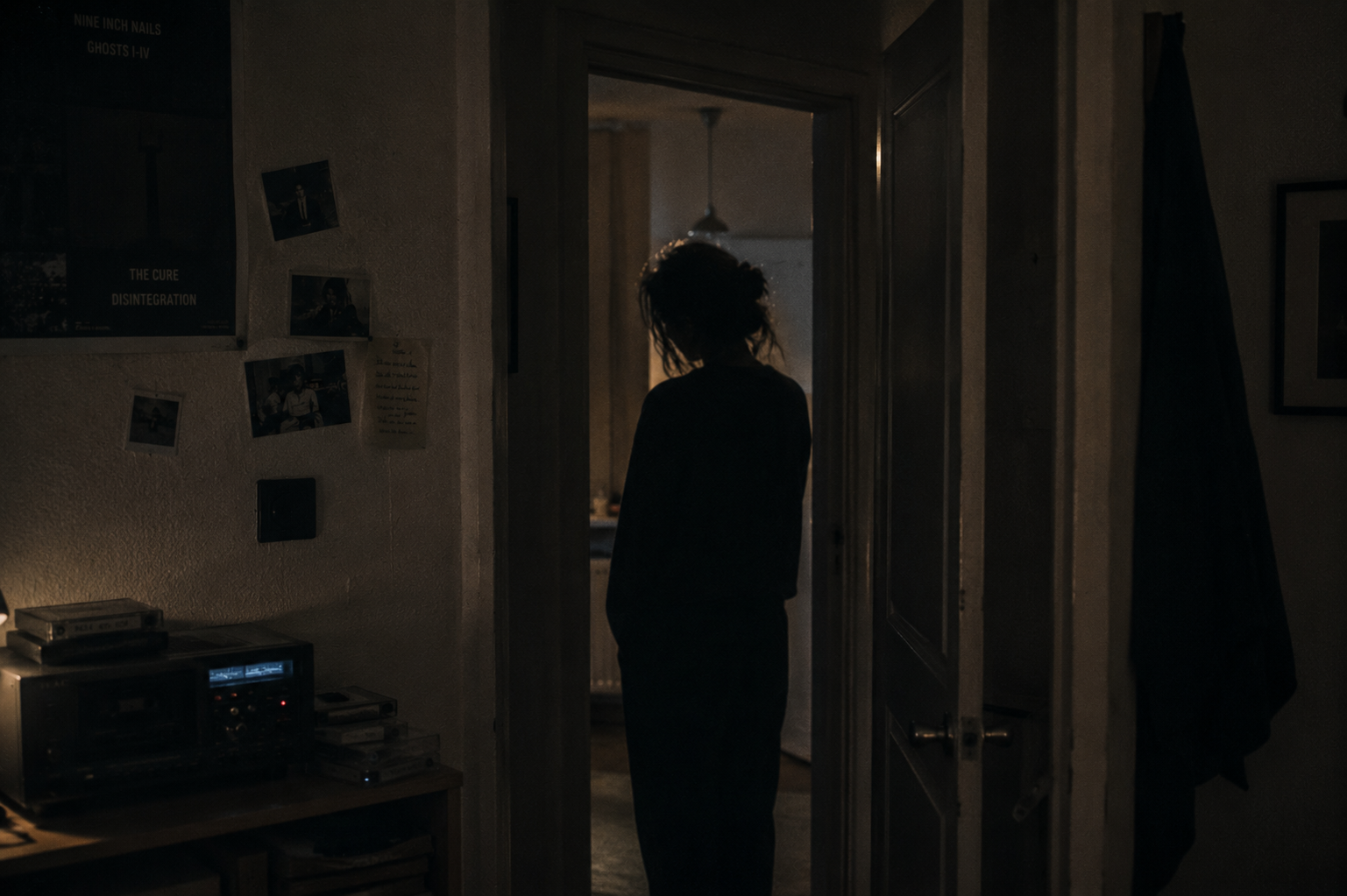 Silhouette of a person standing in an apartment doorway at 04:31 — dark hallway, warm dim room beyond, Nine Inch Nails Ghosts I-IV and The Cure Disintegration posters, polaroids and handwritten notes on the wall, cassette deck with tapes on a low shelf